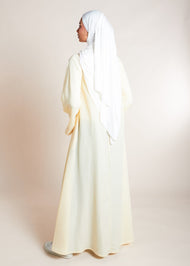 This open pleat abaya in buttercream boasts exquisite neat pleating that cascades down the placket and cuffs, offering a loose yet structured fit for all body types. Perfect as a quick cover-up for everyday outfits, or paired with one of our full slips for a more elegant ensemble.